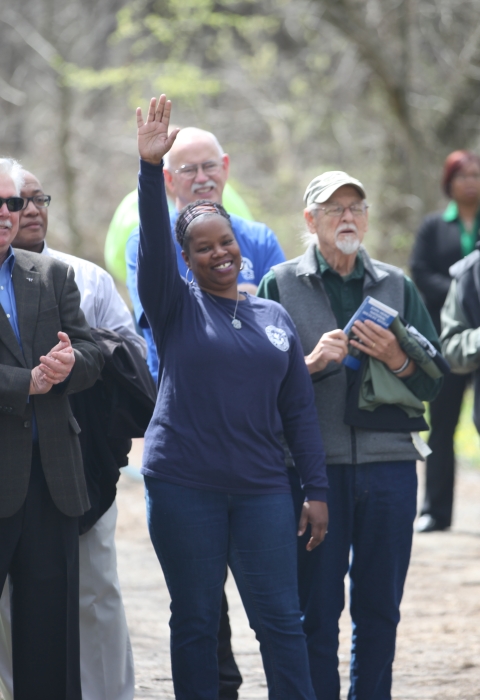 A smiling woman raises her arm high while a group of people standing around her smile at her and applaud.