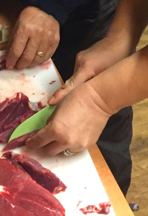 Red caribou meat being cut into slices and cubes on a kitchen table