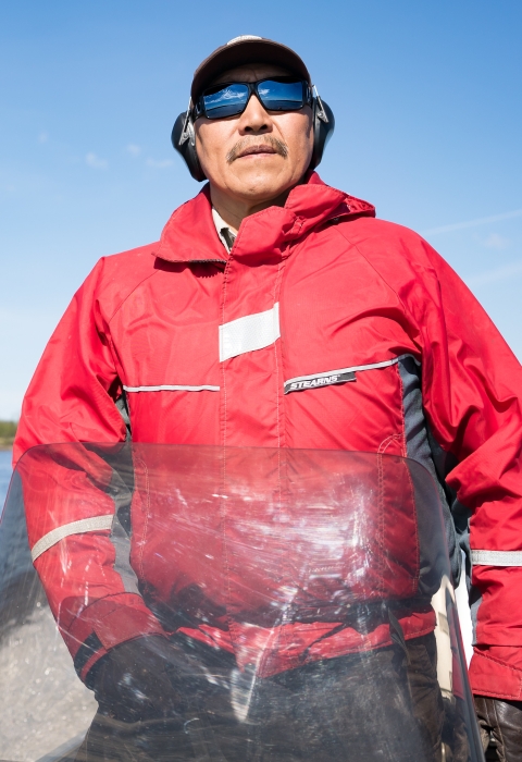 A man in an orange float coat drives a small skiff on a river