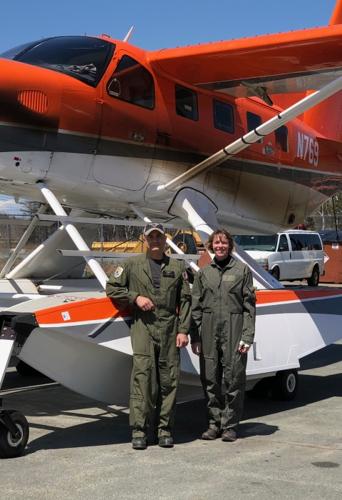 2 people stand in front of an airplane