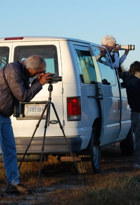 3 people using scopes & binoculars by white van looking for wildlife