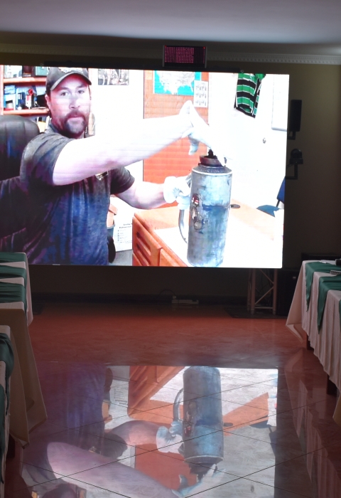 class watches man on video screen with what looks like metal jug