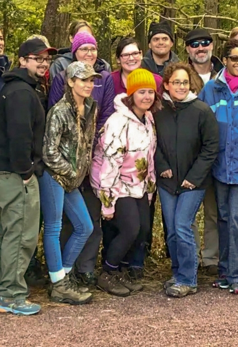 A group of about 20 dressed in warm clothes pose together in a forest
