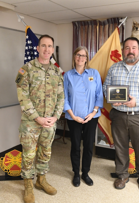 Three people stand together, one holding an award plaque