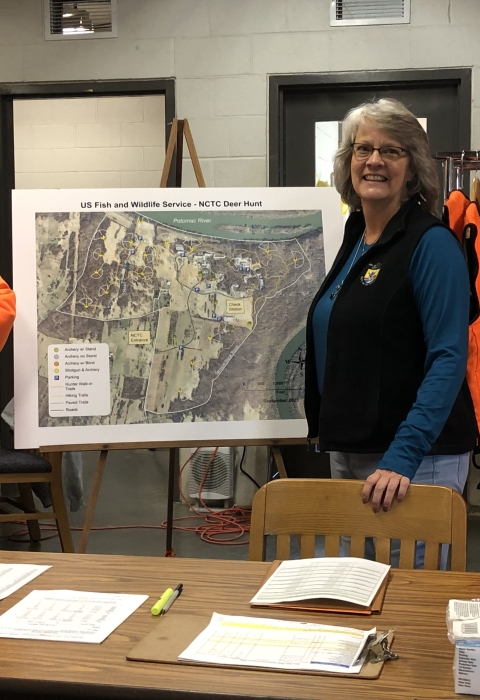 Lowell Haagenson and Lori Bennett inside the NCTC deer check-station surrounded by hunting area maps and blaze orange vests for hunters. 
