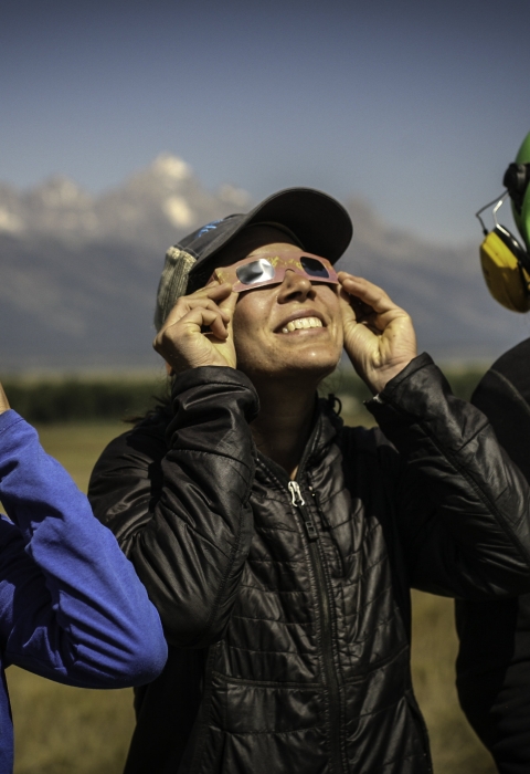Three people wearing special eclipse glasses, stare up