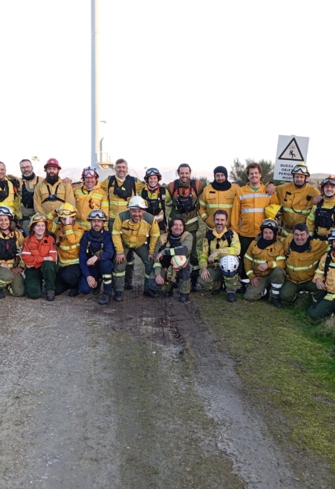 A large group of people in fire gear stand as a group and pose for a photo along what looks to be a dirt road