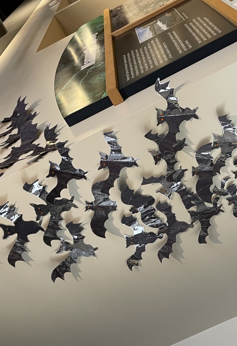 A group of black paper bats flying in formation attached to a wall 