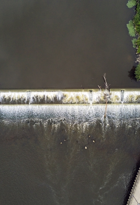 Aerial view of a dam in a dark river with green grass on both side