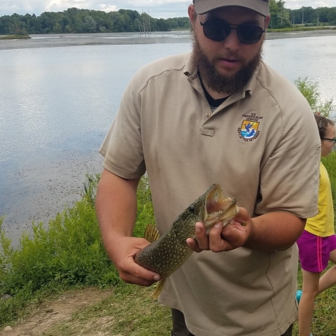 Image of FWS biologist holding a fish next to water.