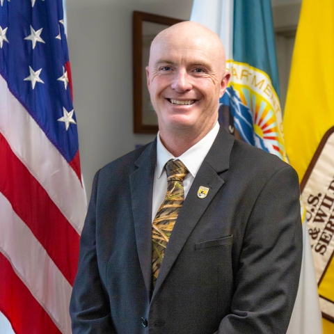 man in suit in front of US, FWS flags