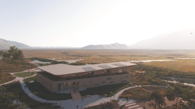 A modern building with various walkways and overlooks adjacent to an large open meadow.