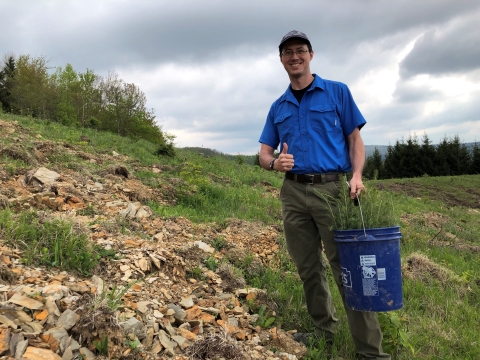a man stands with a thumbs up and a bucket of tree seedlings