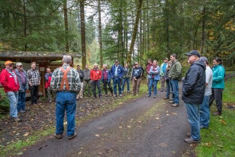 People standing in a circle talking in front of a house in a forest 