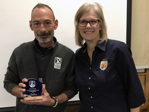 Man in vest with Roger Williams Park Zoo logo holds a round blue award next to a woman in a shirt with a U.S. Fish and Wildlife Service logo