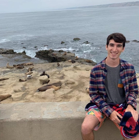 Dimitri sits in front of a beach on a ledge
