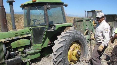 A man in a U.S. Fish and Wildlife Service uniform stands alongside a tractor in an outdoor setting