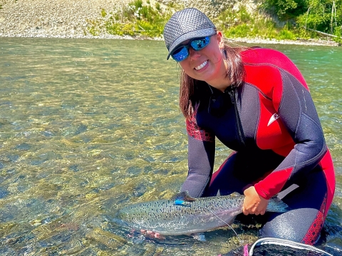 Service intern in river holding a Chinook Salmon with a radio tag on it's dorsal fin.