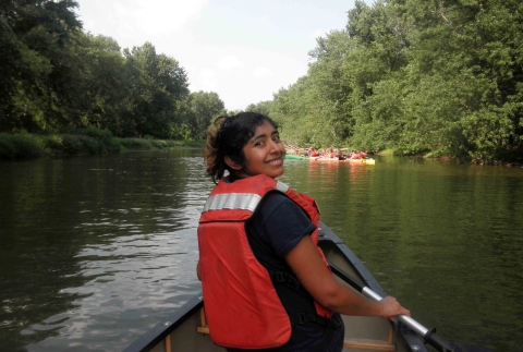 A latina woman wearing an orange personal flotation device canoeing on a river