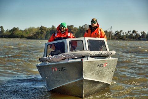 Two men pilot a motored boat on a river