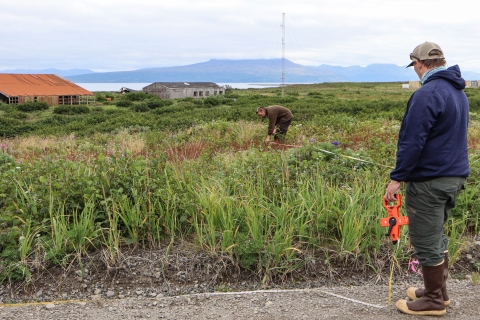 man holding measuring tape while another man bends down to stake the other end of the measuring tape