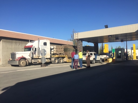 group of people looking at a stopped truck which is transporting boats through a stopping point