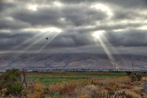 Sun rays shining through dark clouds over a green-and-brown landscape