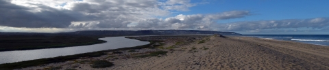A river coming from the left curves to meet the ocean with a sandy beach in the foreground