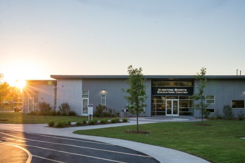 he left side of a brick-and-mortar buidling is illuminated by the sunrise peeping above the treeline.