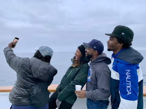 Four members of the organization stand next to each other and take a selfie. The ocean view is in the background.