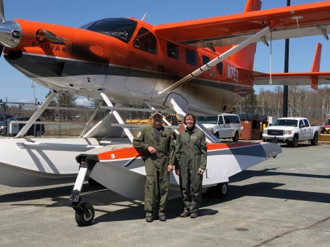 2 people stand in front of an airplane