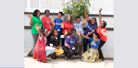 A group of women smiles and waves towards the camera