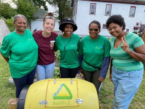 5 people stand with arms around each in front of a yellow barrel-shaped object with the words "groundwork Buffalo" written on it