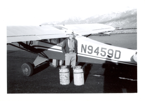 A man stands next to a small aircraft with milk cans of fish to release