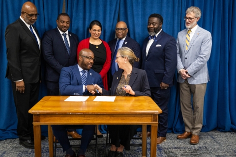6 dressed up people behind 2 at table shaking hands