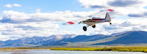 bush plane in the air over river and mountains