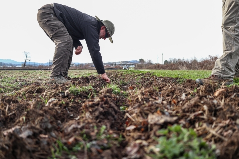 Person bent over, hand in a section of tilled soil, while someone stands nearby