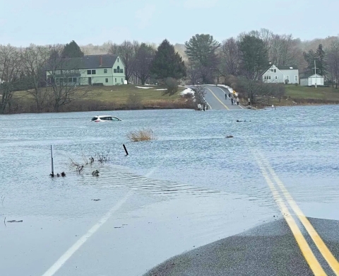 Road bisecting a tidal marsh is flooded with standing water at high tide, as a car is swept off the road into the marsh