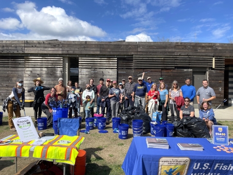 Many people gathered behind tables with trash collecting tools