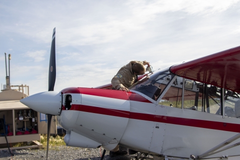 SFWO Cody Smith with a fuel hose putting fuel into the wing tanks of a Top Cub bush plane with a remote fuel station in the background.