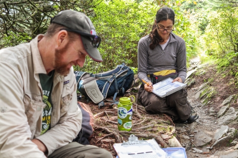 Two biologists beside a trail with clipboards and papers