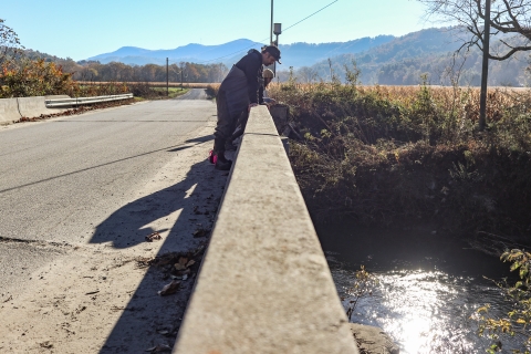Two people standing on a bridge looking down at a river