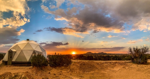 A sunset on a desert with a small dome-shaped building pictured