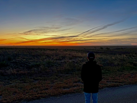 Youth looking off into a field with a orange, yellow and blue sunset