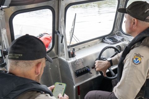 Two Federal Wildlife Officers at the helm of a boat as one looks at a map and gives directions to the other. 