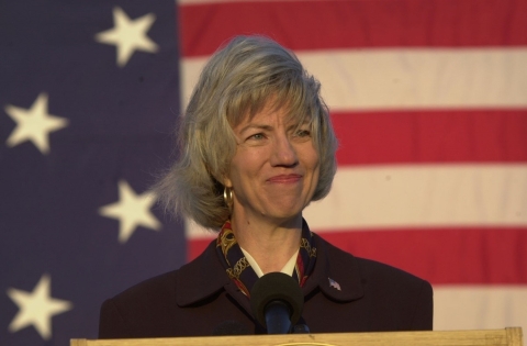 woman stands at a podium with an American flag behind her