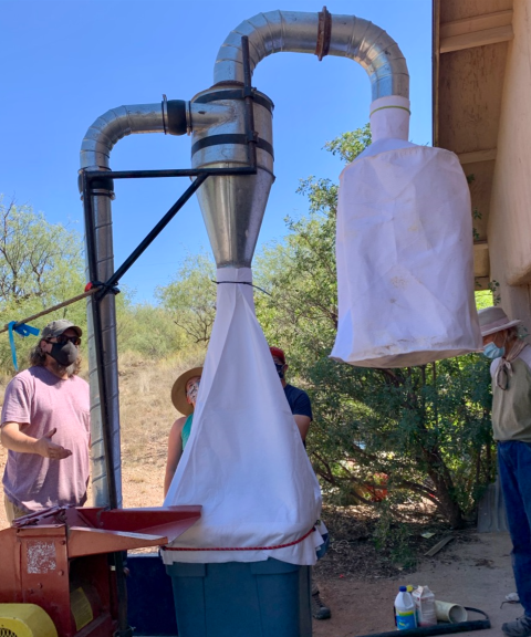 Volunteers standing around a hammer mill outdoors