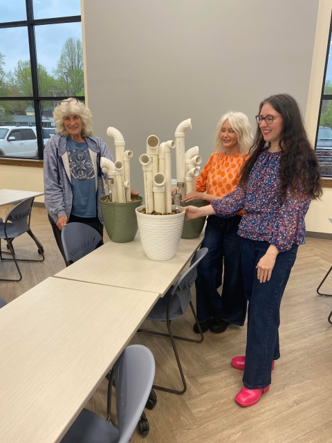 3 women pose with their DIY frog hotels in classroom