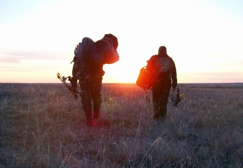 Two hunters cross a prairie at sunrise