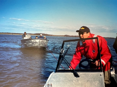 a federal officer at the helm of a river boat drives as his boat is tied to another boat with a family of five people
